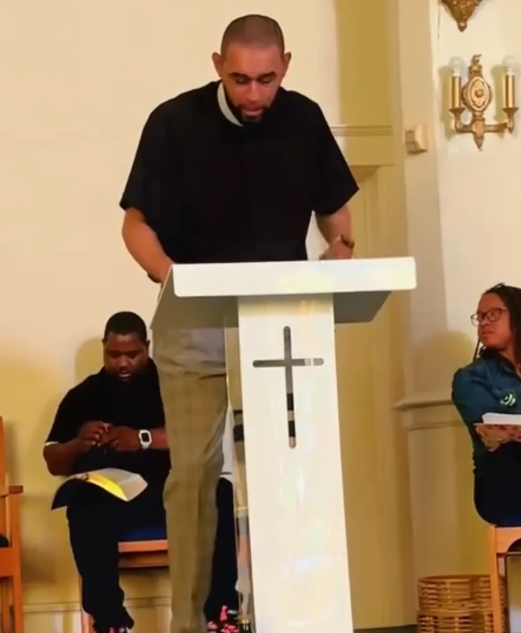 Apostle Marlowe Currie preaching from the white pulpit with a cross cut through it
