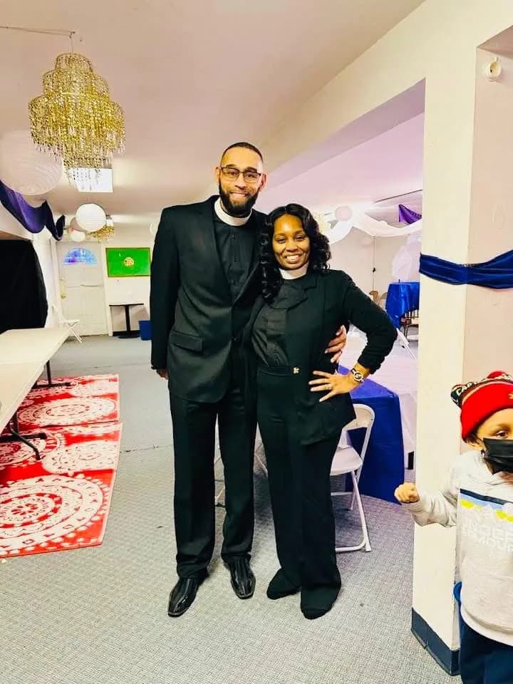 Apostle Marlowe Currie and First Lady Currie in clerical collars, smiling in the fellowship hall