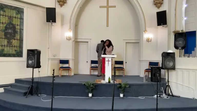 The sanctuary at 4301 Page Blvd: a brass cross in a tall arch, stained glass, and the worship team on the blue-carpeted platform