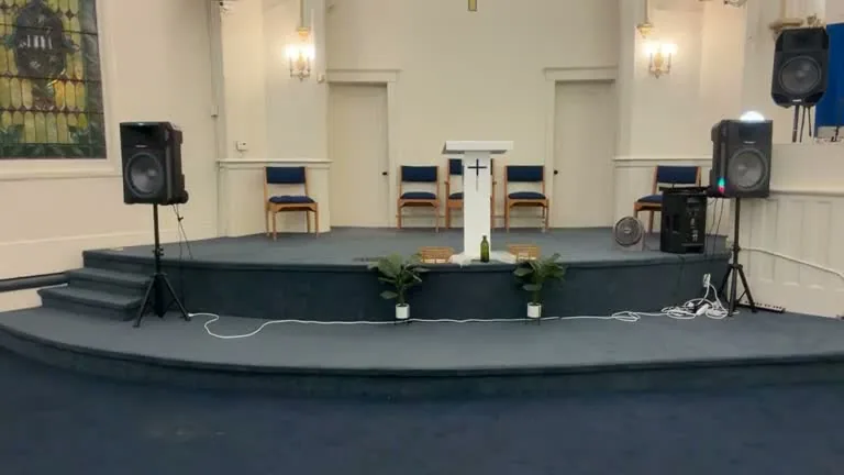 The sanctuary at 4301 Page Blvd: a brass cross in a white arch above a blue-carpeted platform with a white pulpit