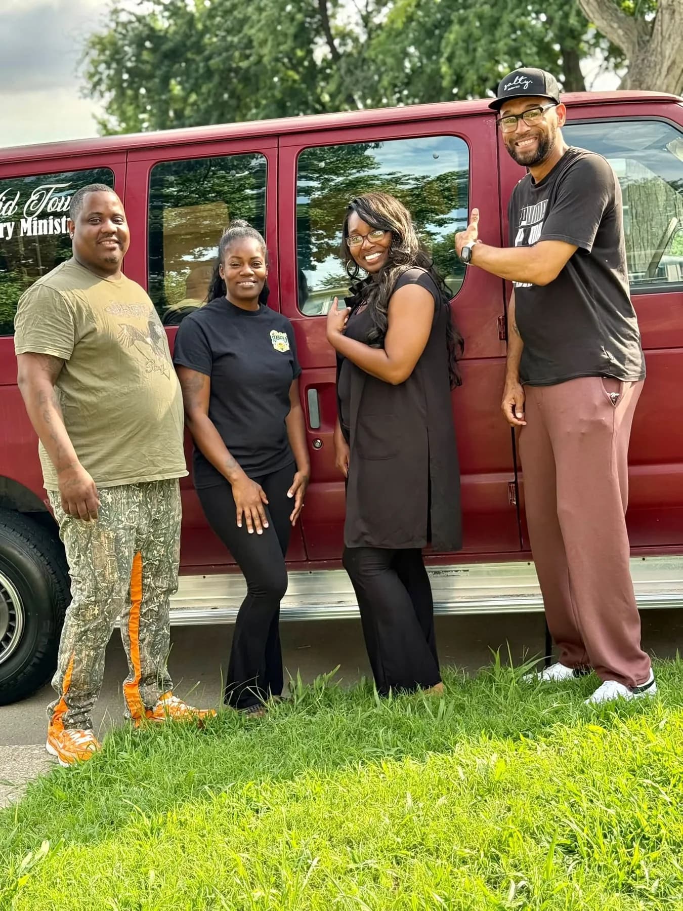 Four members of Currie The Cross Church standing beside the church’s maroon passenger van